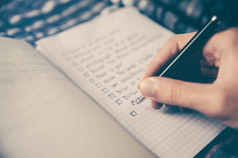 A hand holding a pen on top of a notebook, writing a checklist