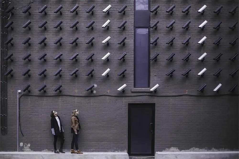 People staring at a large number of CCTV cameras mounted on a building wall